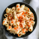 a black bowl filled with a creamy looking elbow macaroni salad topped with shredded carrots